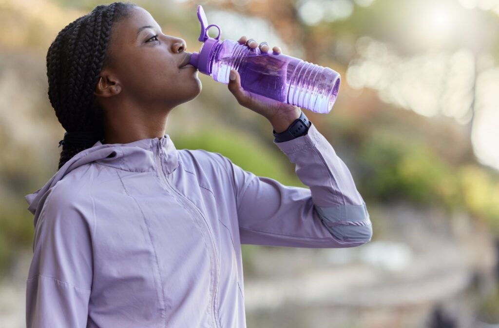 A young runner pauses to drink water from a purple water bottle while out for a jog