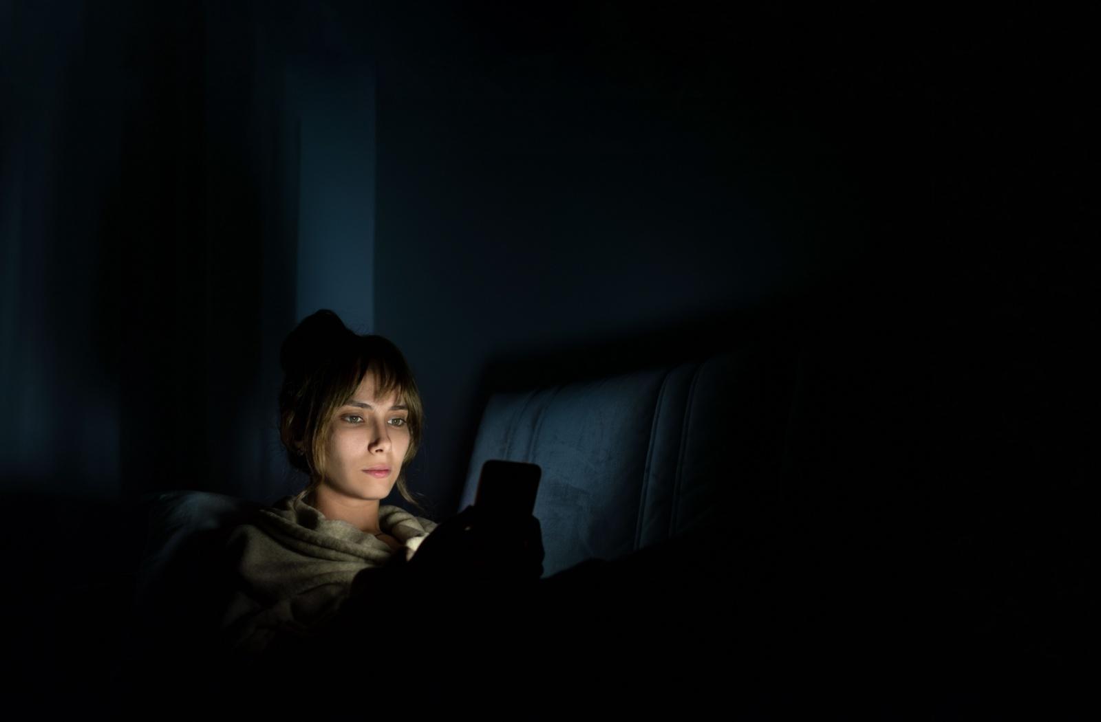 A person sitting in a dark room looking at their phone screen.